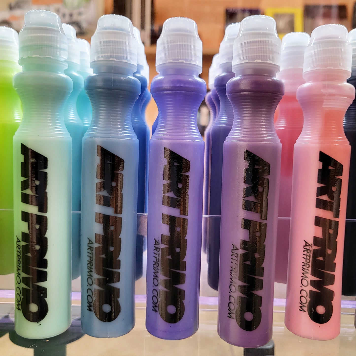 Vertically standing markers reading "ART PRIMO - artprimo.com" on the faces. From left to right colors are bright green, aqua, blue, violet, purple, light pink and black.